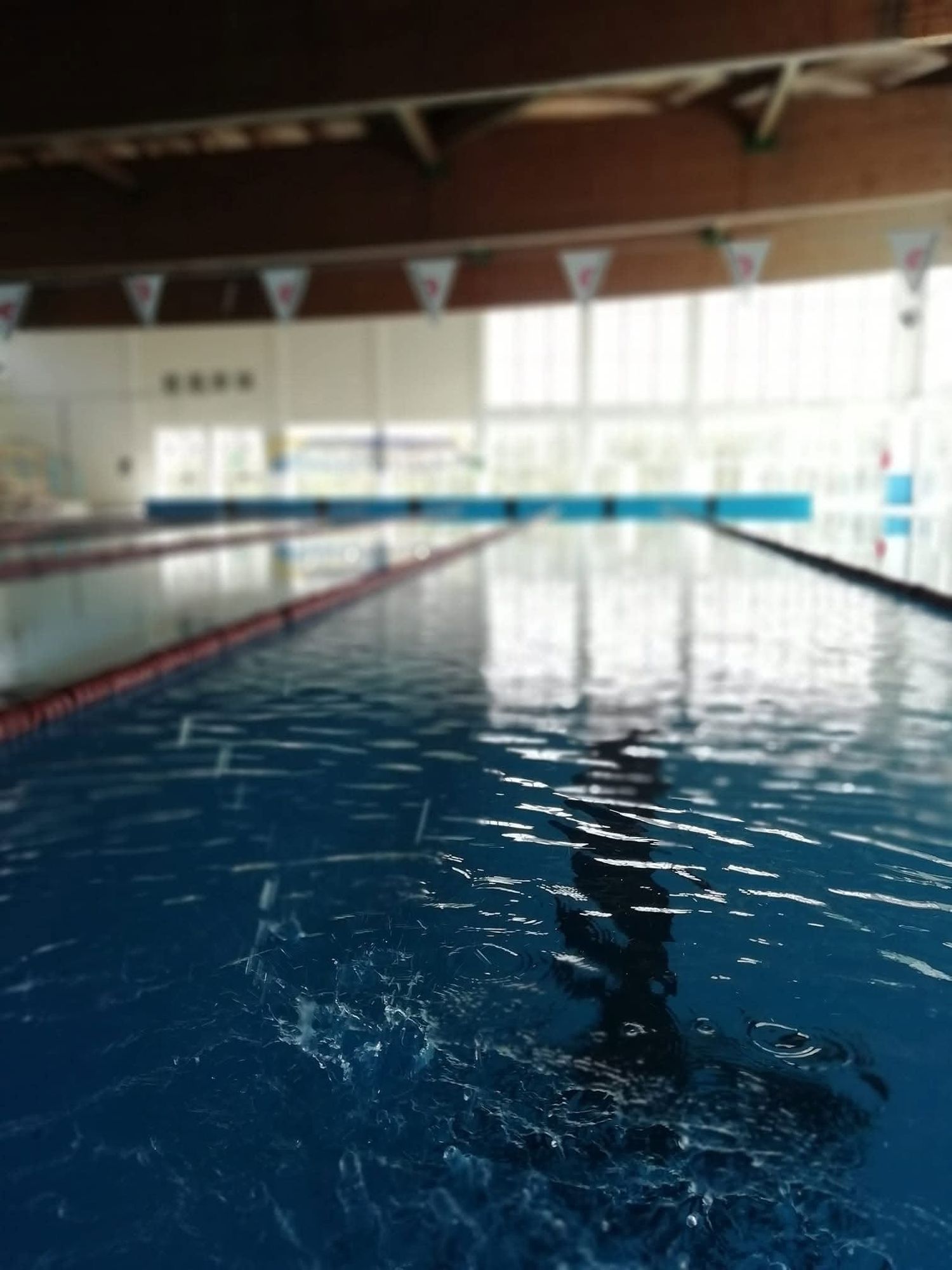 La vasca coperta della piscina comunale di Noto vista dal bordo, con le corsie e la luce che entra dalle vetrate